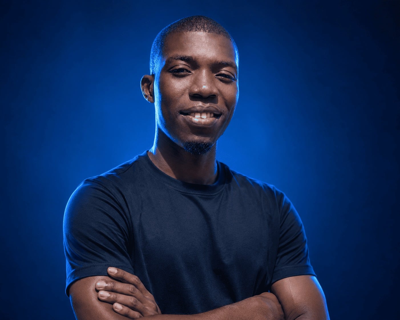 Portrait of Abdoulaye Niang, arms crossed, in a black t-shirt against a deep blue studio background